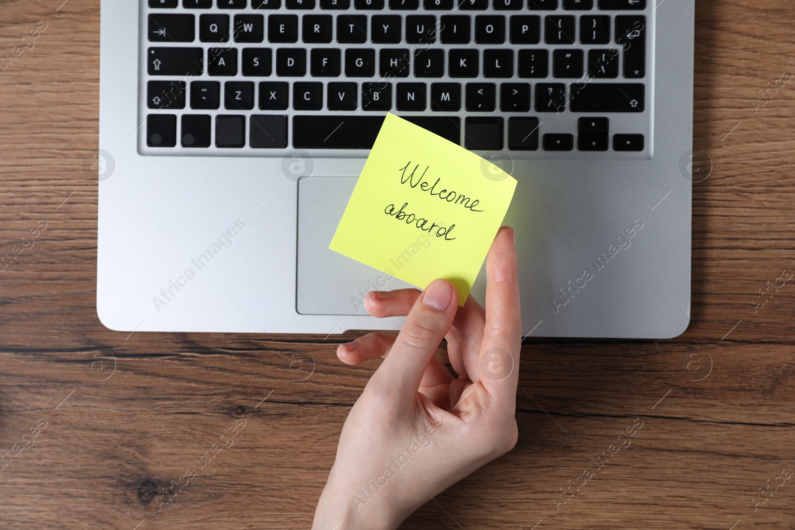 Woman holding paper note with words Welcome Aboard near laptop at wooden table, top view Photo of Woman holding paper note with words Welcome Aboard near laptop at wooden table, top view