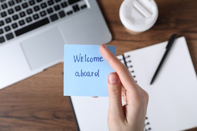 Photo of Woman holding paper note with words Welcome Aboard at wooden table, top view