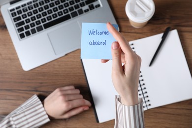 Photo of Woman holding paper note with words Welcome Aboard at wooden table, top view