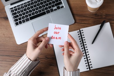 Photo of Woman holding paper note with words Join Our Team at wooden table, top view