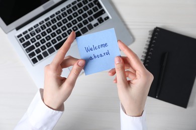 Photo of Woman holding paper note with words Welcome Aboard at light wooden table, top view
