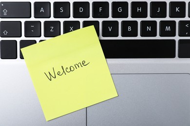 Photo of Paper note with word Welcome on laptop, top view