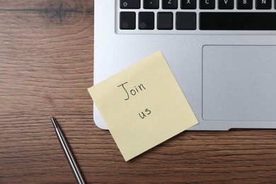 Photo of Paper note with words Join Us, laptop and pen on wooden table, flat lay