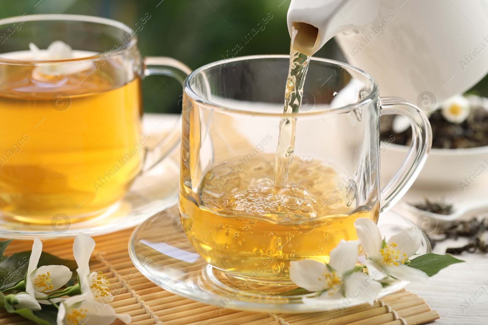 Pouring tasty jasmine tea into cup on white wooden table, closeup Photo of Pouring tasty jasmine tea into cup on white wooden table, closeup