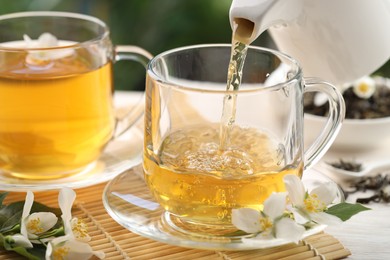 Photo of Pouring tasty jasmine tea into cup on white wooden table, closeup