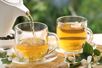 Photo of Pouring tasty jasmine tea into cup on white wooden table, closeup