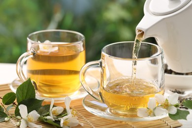 Photo of Pouring tasty jasmine tea into cup on white wooden table, closeup