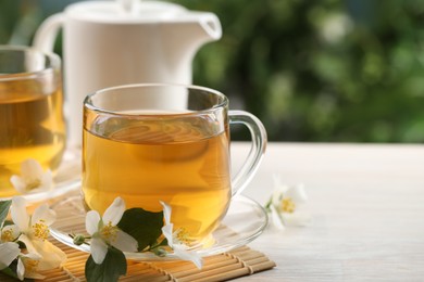 Photo of Tasty jasmine tea in cups, teapot and flowers at white wooden table, closeup. Space for text