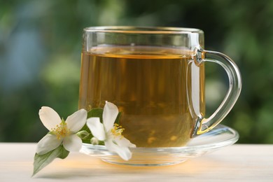 Photo of Tasty jasmine tea in cup and flowers at white wooden table, closeup