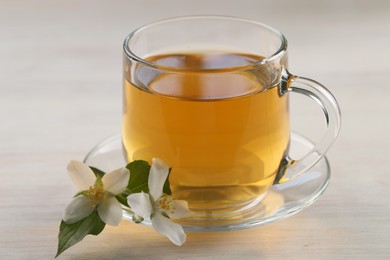 Photo of Tasty jasmine tea in cup and flowers at white wooden table, closeup