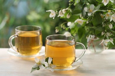 Photo of Tasty jasmine tea in cups and flowers at white wooden table, closeup