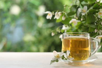 Photo of Tasty jasmine tea in cup and flowers at white wooden table, closeup. Space for text