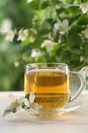 Photo of Tasty jasmine tea in cup and flowers at white wooden table, closeup