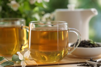 Photo of Tasty jasmine tea in cups, teapot, dry leaves and flowers at white wooden table, closeup