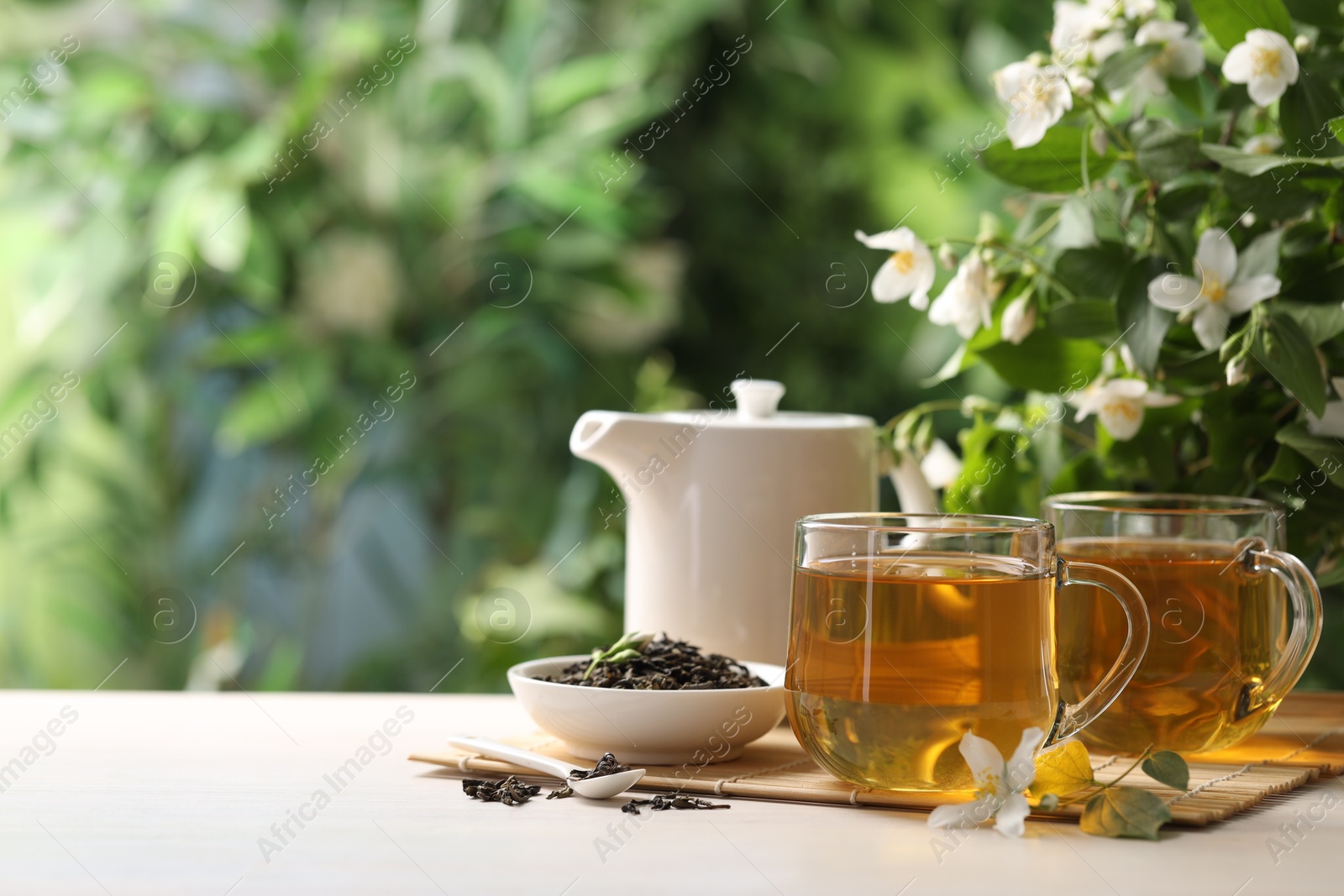 Tasty jasmine tea in cups, teapot, dry leaves and flowers at white wooden table, closeup. Space for text Photo of Tasty jasmine tea in cups, teapot, dry leaves and flowers at white wooden table, closeup. Space for text