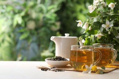 Photo of Tasty jasmine tea in cups, teapot, dry leaves and flowers at white wooden table, closeup. Space for text