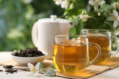 Photo of Tasty jasmine tea in cups, teapot, dry leaves and flowers at white wooden table, closeup