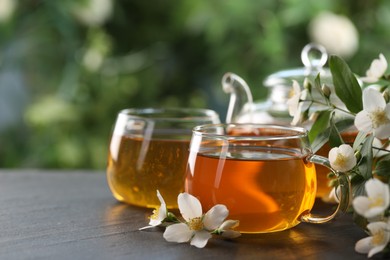 Photo of Tasty jasmine tea in cups, teapot and flowers on black table, closeup. Space for text