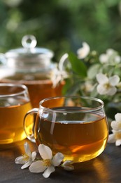 Photo of Tasty jasmine tea in cups, teapot and flowers on black table, closeup