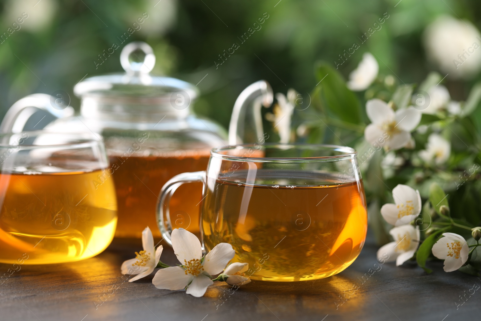 Tasty jasmine tea in cups, teapot and flowers on black table, closeup Photo of Tasty jasmine tea in cups, teapot and flowers on black table, closeup