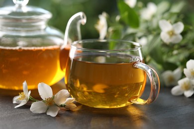 Photo of Tasty jasmine tea in cup, teapot and flowers on black table, closeup