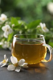 Photo of Tasty jasmine tea in cup and flowers on black table, closeup