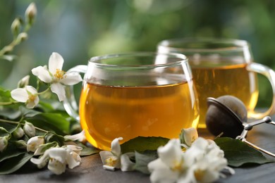 Photo of Tasty jasmine tea in cups, dry leaves and flowers on black table, closeup
