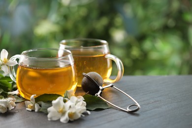 Photo of Tasty jasmine tea in cups, dry leaves and flowers on black table, closeup. Space for text