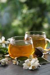 Photo of Tasty jasmine tea in cups, dry leaves and flowers on black table, closeup