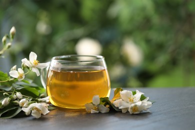 Photo of Tasty jasmine tea in cup and flowers on black table, closeup. Space for text