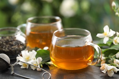 Photo of Tasty jasmine tea in cups, dry leaves and flowers on black table, closeup
