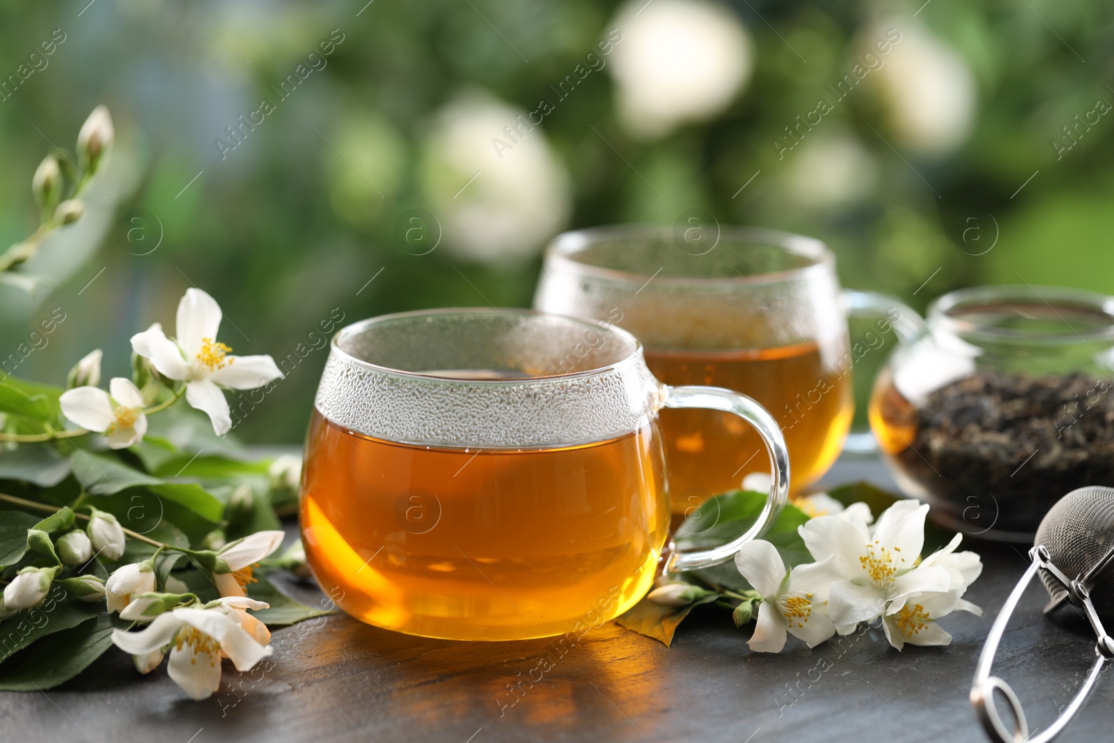Tasty jasmine tea in cups, dry leaves and flowers on black table, closeup Photo of Tasty jasmine tea in cups, dry leaves and flowers on black table, closeup