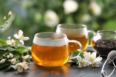 Photo of Tasty jasmine tea in cups, dry leaves and flowers on black table, closeup