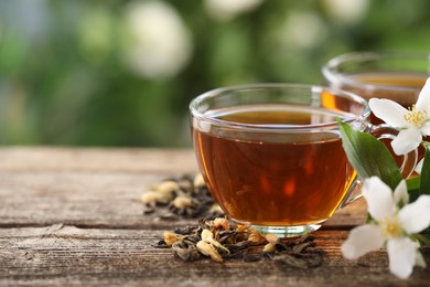 Photo of Tasty jasmine tea in cups, dry leaves and flowers on wooden table, closeup. Space for text