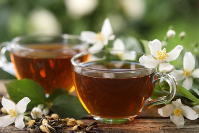 Photo of Tasty jasmine tea in cups, dry leaves and flowers on wooden table, closeup