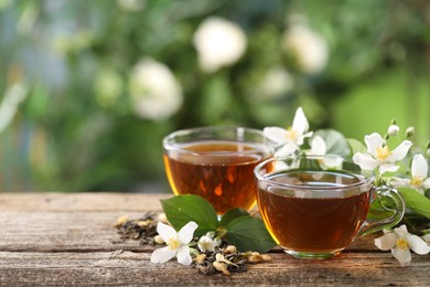 Photo of Tasty jasmine tea in cups, dry leaves and flowers on wooden table, closeup. Space for text