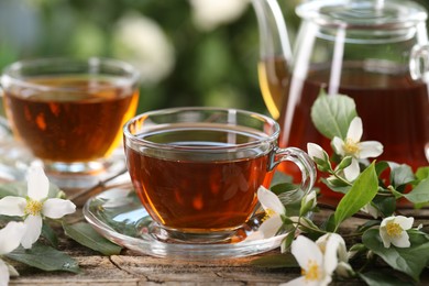 Photo of Tasty jasmine tea in cups, teapot and flowers on wooden table, closeup