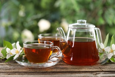 Photo of Tasty jasmine tea in cups, teapot and flowers on wooden table, closeup