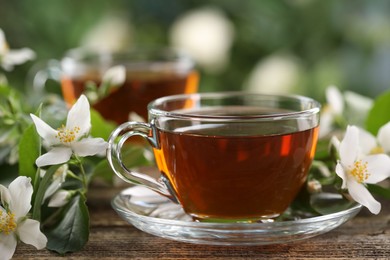 Photo of Tasty jasmine tea in cups and flowers on wooden table, closeup