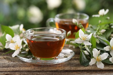 Photo of Tasty jasmine tea in cups and flowers on wooden table, closeup