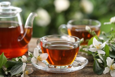 Photo of Tasty jasmine tea in cups, teapot and flowers on wooden table, closeup
