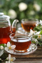 Photo of Tasty jasmine tea in cups, teapot and flowers on wooden table, closeup
