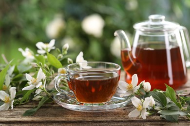 Photo of Tasty jasmine tea in cup, teapot and flowers on wooden table, closeup