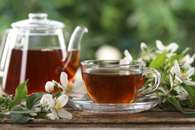 Photo of Tasty jasmine tea in cup, teapot and flowers on wooden table, closeup