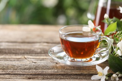 Photo of Tasty jasmine tea in cup and flowers on wooden table, closeup. Space for text