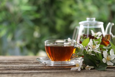 Photo of Tasty jasmine tea in cup, teapot and flowers on wooden table, closeup. Space for text
