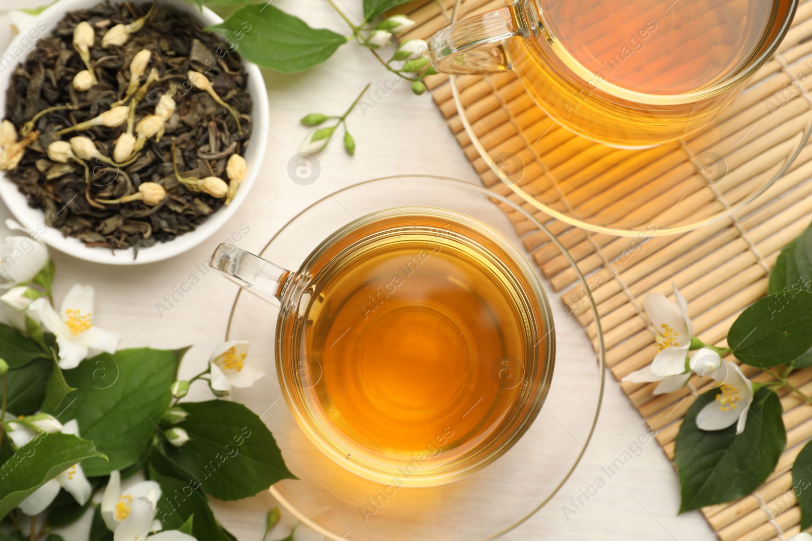 Tasty jasmine tea in cups, dry leaves and flowers on white wooden table, flat lay Photo of Tasty jasmine tea in cups, dry leaves and flowers on white wooden table, flat lay