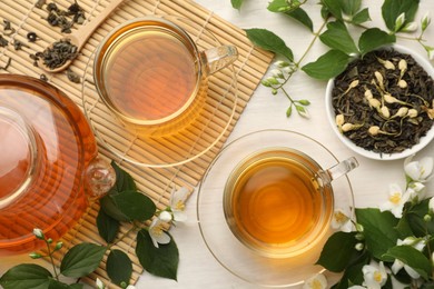 Photo of Tasty jasmine tea in cups, teapot, dry leaves and flowers on white wooden table, flat lay