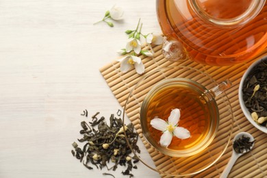 Photo of Tasty jasmine tea in cup, teapot, dry leaves and flowers on white wooden table, flat lay. Space for text