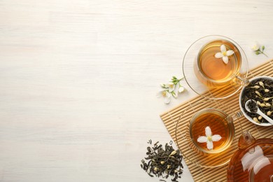 Photo of Tasty jasmine tea in cups, teapot, dry leaves and flowers on white wooden table, flat lay. Space for text
